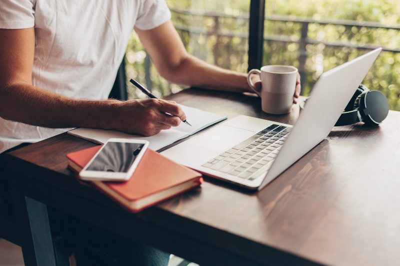 Personne travaillant sur un ordinateur portable avec une tablette et un carnet à ses côtés, ambiance professionnelle.