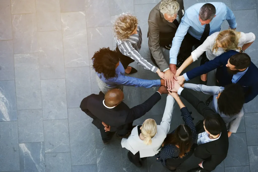 Photo d'une équipe diverse réunie en cercle, mains jointes au centre pour symboliser la cohésion et l’engagement