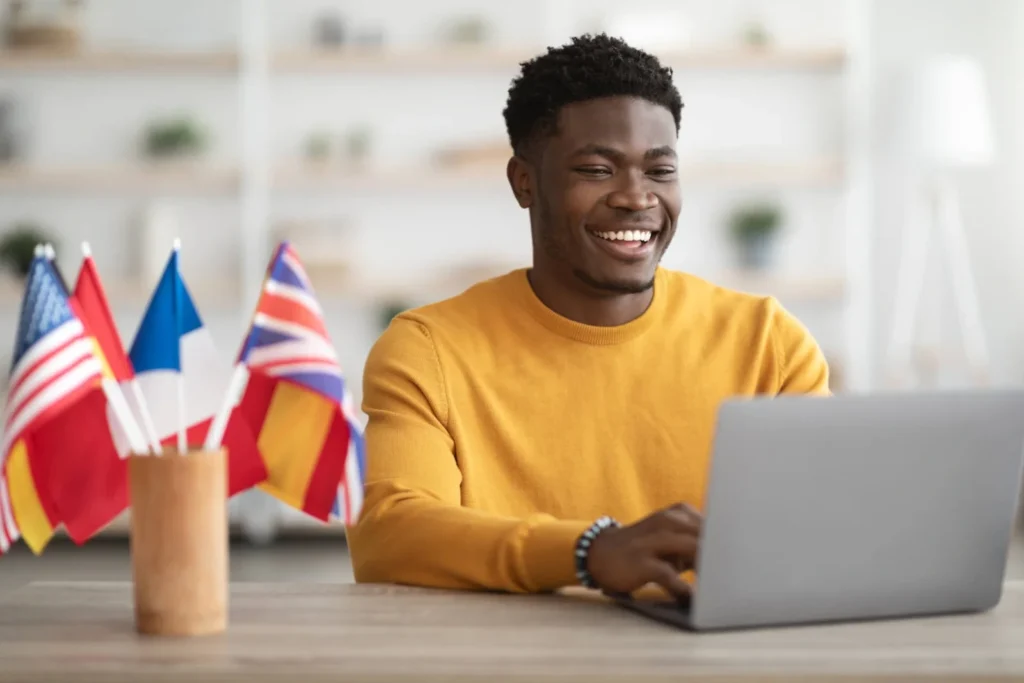 Jeune homme étudiant en ligne avec un ordinateur portable et des drapeaux internationaux