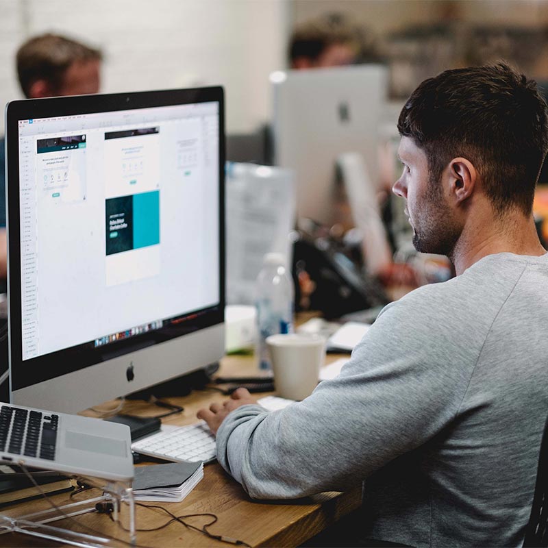 Homme concentré travaillant sur un site internet, devant un double écran dans un bureau partagé.
